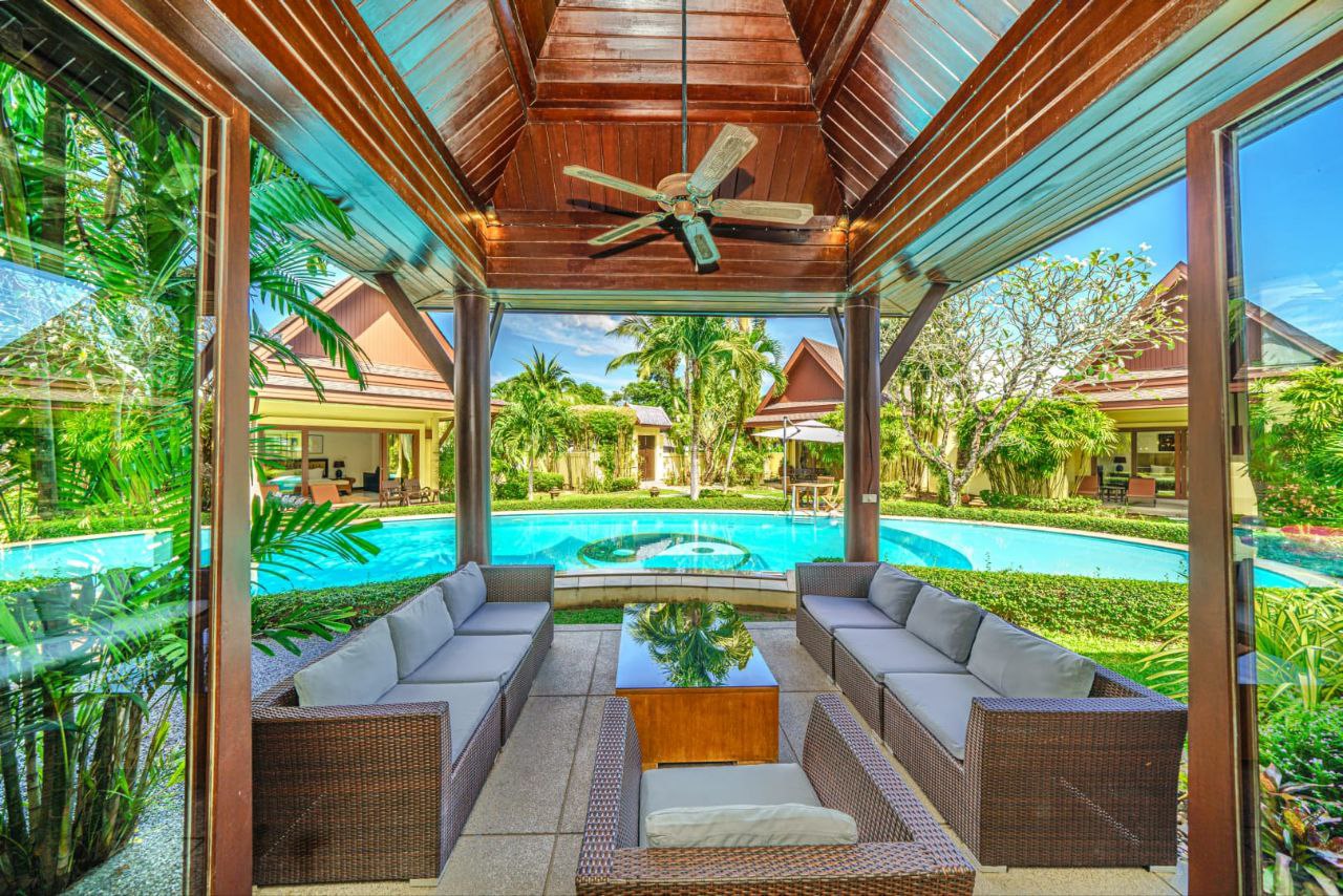 Outdoor lounge with wicker sofas facing a swimming pool and tropical garden at The Himmaphan Phuket.